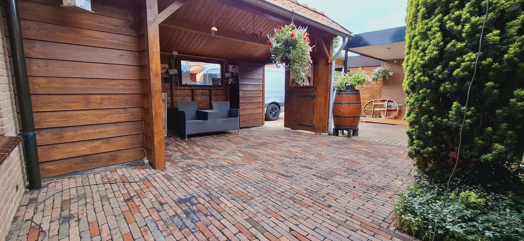 Houten overkapping met loungeset, hanging basket en een terras van gebakken klinkers