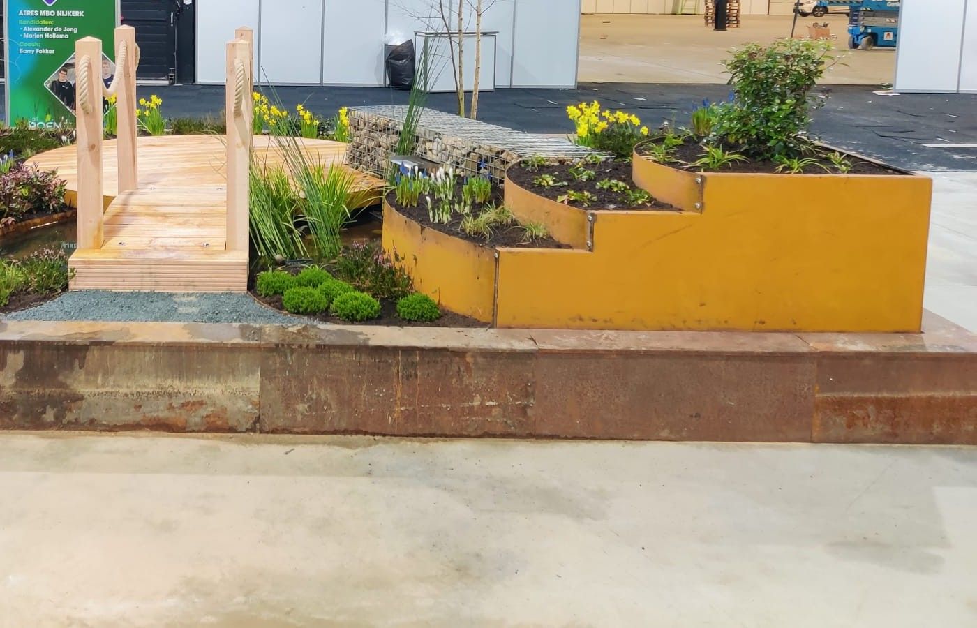De wedstrijdtuin van Marien en Alexander in de beurshal, met houten brug, schanskorfbank, cortenstalen bakken en narcissen