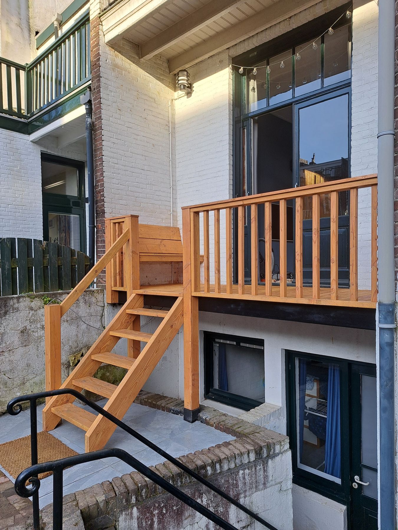 Houten balkon met trap en leuning aan de achterzijde van een wit geschilderd huis